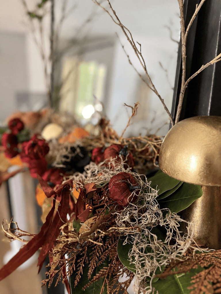 Close-up of Spanish moss, burgundy pumpkins, greenery and a gold mushroom on a fall mantle