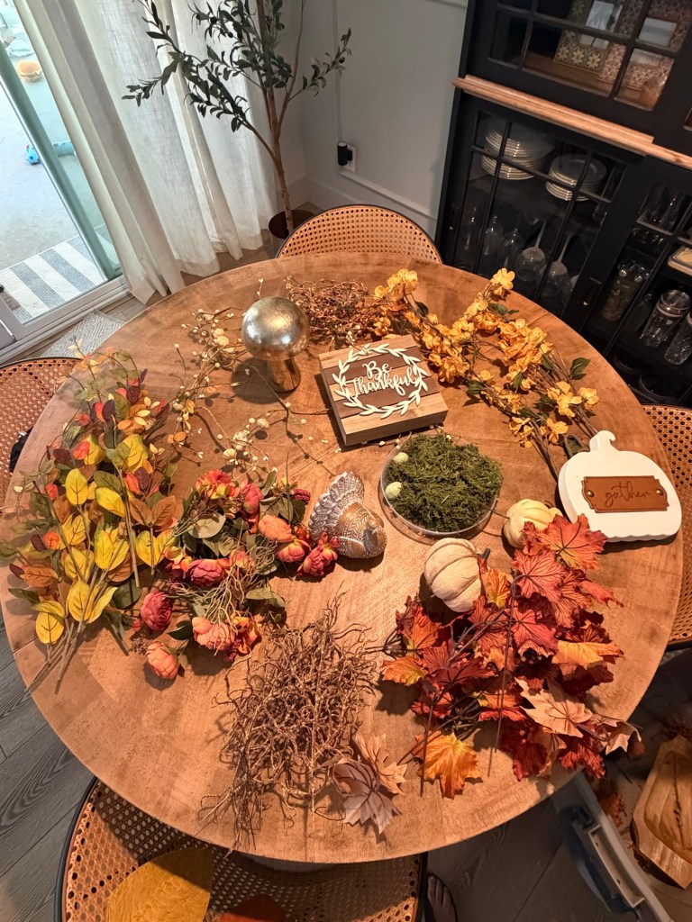 Fall decor and floral stems laid out on dining table before decorating